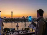 Mężczyzna z plecakiem trzyma telefon z napisem "5G CONNECT" na tle zachodzącego słońca nad Nilem, z widocznymi piramidami w Egipcie. eSIM Egipt zapewnia łączność.