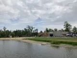 Spokojne jezioro małe żnińskie z piaszczystą plażą, budynkiem CSW i zielenią w tle.