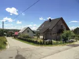 Dwa domy w budowie, jeden gotowy, na tle błękitnego nieba z chmurami. Widać drogę i zieleń. Różne kategorie gleby widoczne na poboczu.