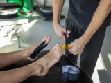 Fizjoterapeuta zakłada czarny plaster na stopę pacjenta, obok leży rolka plastra.