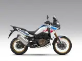 Nowy motocykl Honda Africa Twin 1100 w białym malowaniu z niebieskimi i czerwonymi akcentami, gotowy na przygodę.