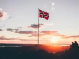 Zachód słońca w Norwegii. Dwie osoby siedzą na skale, patrząc na krajobraz. Flaga Norwegii powiewa na maszcie. Czy do Norwegii można lecieć na dowód osobisty?