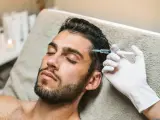 Mężczyzna leży z zamkniętymi oczami, gdy kosmetyczka wykonuje zabieg botoks po solarium.