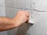 Main d'une personne appliquant du mastic sur les joints d'une salle de bain.
