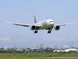 Emirates Boeing 777 zbliża się do lądowania. W tle widać przemysłowy krajobraz i inne samoloty na niebie, sugerujące ruch lotniczy, być może związane z dżerba loty.