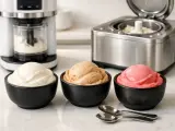 Drei Schalen mit cremigem Eis: Vanille, Karamell und Erdbeere. Daneben Eismaschinen, die das Eis wie Sahne zubereiten.