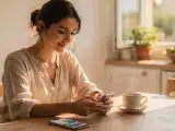 Mujer sonríe usando su móvil, con una taza de café y un gráfico en pantalla. Ideal para un programa para hacer presupuestos gratis.