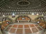 Wnętrze Hali Stulecia podczas zwiedzania. Widok na betonową kopułę, łuki i rzędy pomarańczowych krzeseł.