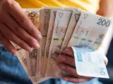 Dłonie trzymają plik banknotów 200 zł i 50 zł. Jak egzekwować obowiązek naprawienia szkody, gdy sprawca nie chce zapłacić?