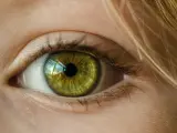 Zielona soczewka oka z refleksami światła, otoczona jasną skórą i blond włosami.