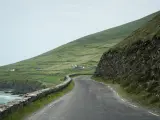 A winding road along the coast of Ireland, perfect for renting a car and exploring the dramatic green hills and stone walls.