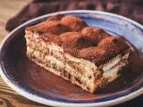 Pyszny kawałek tiramisu z mascarpone, posypany kakao, na niebieskim talerzu. Idealny na deser.