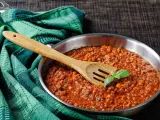 Un saporito ragù di cinghiale in padella, pronto per condire la pasta. Un cucchiaio di legno e una fogliolina di basilico completano la scena.