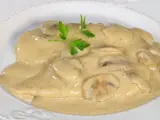 Pollo cremoso con champiñones y perejil en un plato blanco.