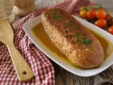Polpettone in padella dorato, guarnito con erba cipollina, servito su un piatto bianco con salsa. Accanto, una spatola di legno e pomodorini.