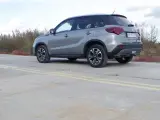 Szary Suzuki Vitara Hybrid z czarnym dachem stoi na betonowej nawierzchni z żółtymi pasami.