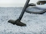 Vacuum cleaner head on a fluffy grey rug, demonstrating how to wash a rug by removing dust and debris.