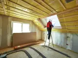 Operaio in piedi su una scala per isolare il tetto di una mansarda con materiale isolante giallo.