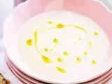 En krämig vit sparrissoppa med en virvel av olivolja i en rosa skål. Serveras med ett kryddigt bröd.