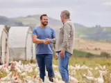 Dwóch rolników wita się na farmie z kurami, symbolizującym sukces w hodowli i troskę o klasy ziemi.