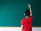 Chłopiec pisze kredą na tablicy, zastanawiając się, przed jakimi spójnikami stawiamy przecinek.