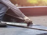 Hand mit Handschuh legt neue Dachpappe an. Alte Dachpappe entsorgen ist der nächste Schritt.