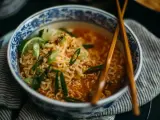 Aksamitny makaron lau thai w misce z niebieskimi zdobieniami, udekorowany szczypiorkiem, chili i limonką.