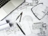 Na biurku architekta leżą plany budowlane, laptop, okulary i cyrkiel. Trwają prace nad przedmiarem robót.