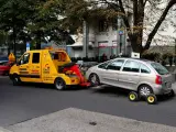 Żółta laweta holuje srebrny samochód, który zapewne dostał mandat za złe parkowanie.