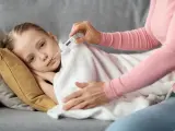 Chore dziecko z gorączką może iść na dwór? Mama mierzy temperaturę chorej córce leżącej pod kocem.