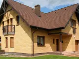 Nowy dom z żółtej cegły, z brązowym dachem i kominem. Widoczny cokół, balkon i wejście zadaszone.