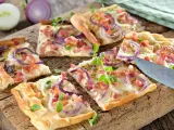 Kawałki pizzy z cebulą i boczkiem na drewnianej desce.