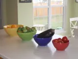 Miseczki w kolorach pastelowych: żółta z pomarańczami, zielona z pomidorkami, niebieska z bakłażanem i czerwona z pomidorkami.