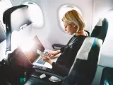 Kobieta pracuje na laptopie i trzyma telefon, zastanawiając się, czy w samolocie można ładować telefon.