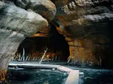 Drewniany pomost prowadzi przez wodę w skalnej grocie. To część malowniczej trasy przez Błędne Skały, gdzie natura tworzy niezwykłe formacje.
