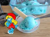 Schlumpfine genießt engelblaues Eis. Ein Handmixer und ein Waffelblatt liegen daneben.