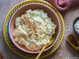 Cremiger Milchreis, bestreut mit Zimt, wartet in einer Schale auf sein Milchreis Rezept. Daneben liegen Reiskörner und Zimtstangen.
