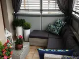 Przytulna zabudowa balkonu w bloku: rattanowy narożnik, poduszki w geometryczne wzory, rośliny i ozdobna latarenka tworzą relaksującą przestrzeń.