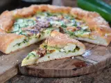 Leckeres Zucchini Pizza Rezept auf einem Holzbrett, mit einem Stück abgetrennt.