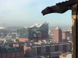 Blick über Hamburg mit der Elbphilharmonie, gesehen durch ein Fenster des Mahnmals St. Nikolai. Ein Wasserspeier wacht über die Stadt.