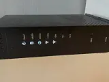 Czarny router Arris TG2492 z widocznym przyciskiem WPS i wskaźnikami stanu: Power, US/DS, Online, 2.4 GHz, 5 GHz, Tel 1, Tel 2.