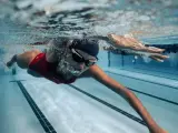 Une femme en maillot de bain rouge nage en crawl, lunettes de natation sur le nez. Sa **natation transformation physique femme** est visible sous l'eau.