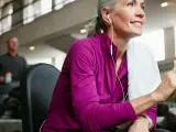 Kobieta w słuchawkach i sportowej bluzce odpoczywa na siłowni, pijąc wodę. Ćwiczenia pomagają zredukować **tłuszcz trzewny**.