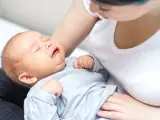 Płaczący noworodek w ramionach mamy. Szukamy odpowiedzi, co na kolki u noworodka, by ulżyć maluszkowi.