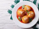 Quattro arancini di riso dorati, cosparsi di parmigiano e serviti su un letto di salsa di pomodoro, guarniti con basilico fresco.