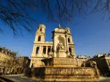 Fuente monumental frente a la iglesia de Saint Sulpice, con leones de piedra y una estatua central bajo un cielo azul claro.