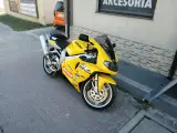 Żółty motocykl Suzuki TL1000R z naklejkami sponsorów, zaparkowany na chodniku.