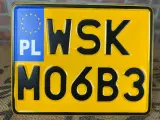 Żółta tablica rejestracyjna z czarnymi znakami "WSK MO6B3" i niebieskim polem "PL" z gwiazdkami UE.