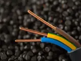 Trzy miedziane żyły kabla elektrycznego, w izolacjach brązowej, żółto-zielonej i niebieskiej, na tle granulatów tworzywa sztucznego. Idealne do instalacji IP20.