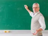 Doświadczony nauczyciel akademicki z kredą w dłoni, tłumaczy coś przy zielonej tablicy.